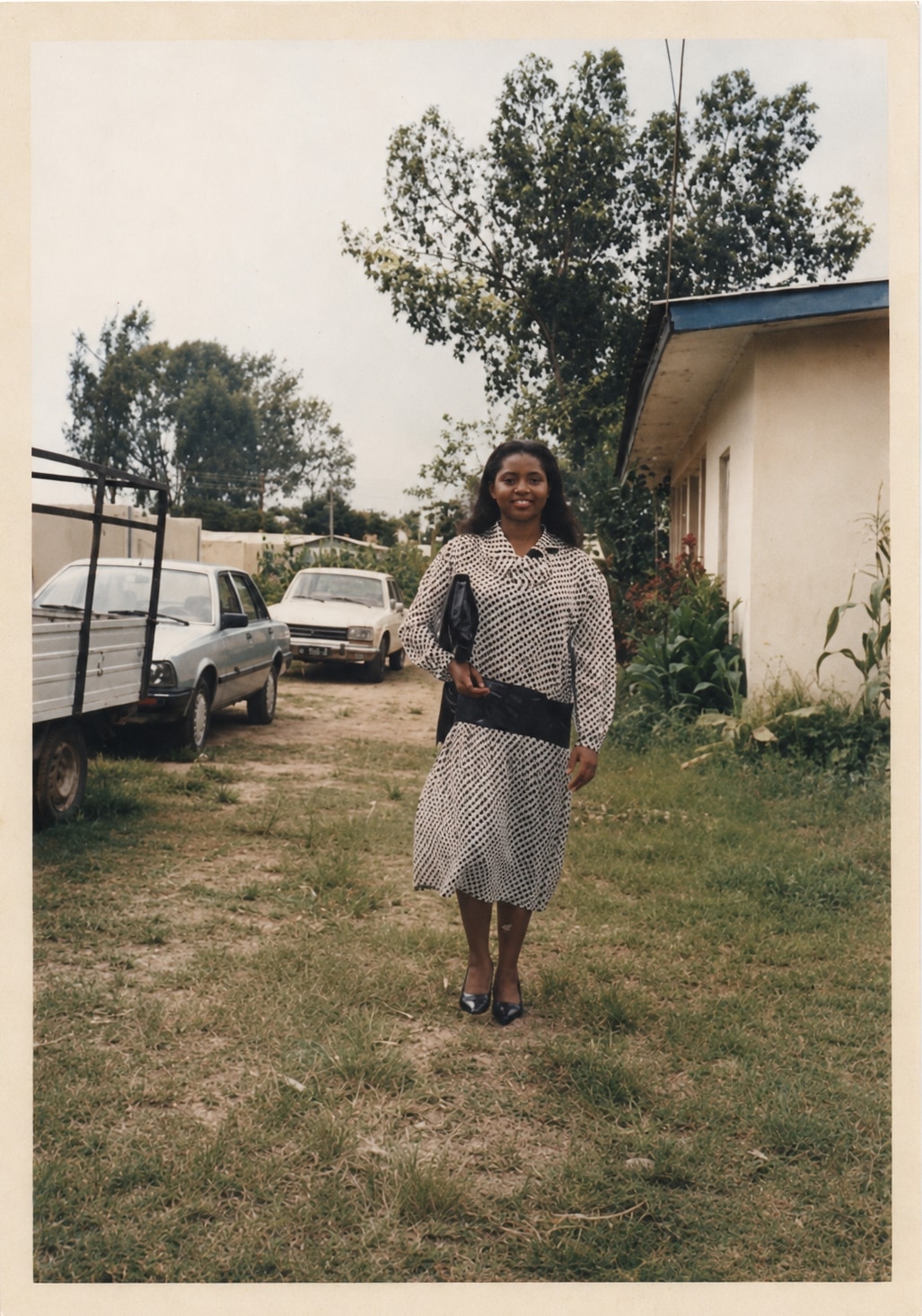 Oby walking on grass in a patterned dress, cars and a bungalow behind her