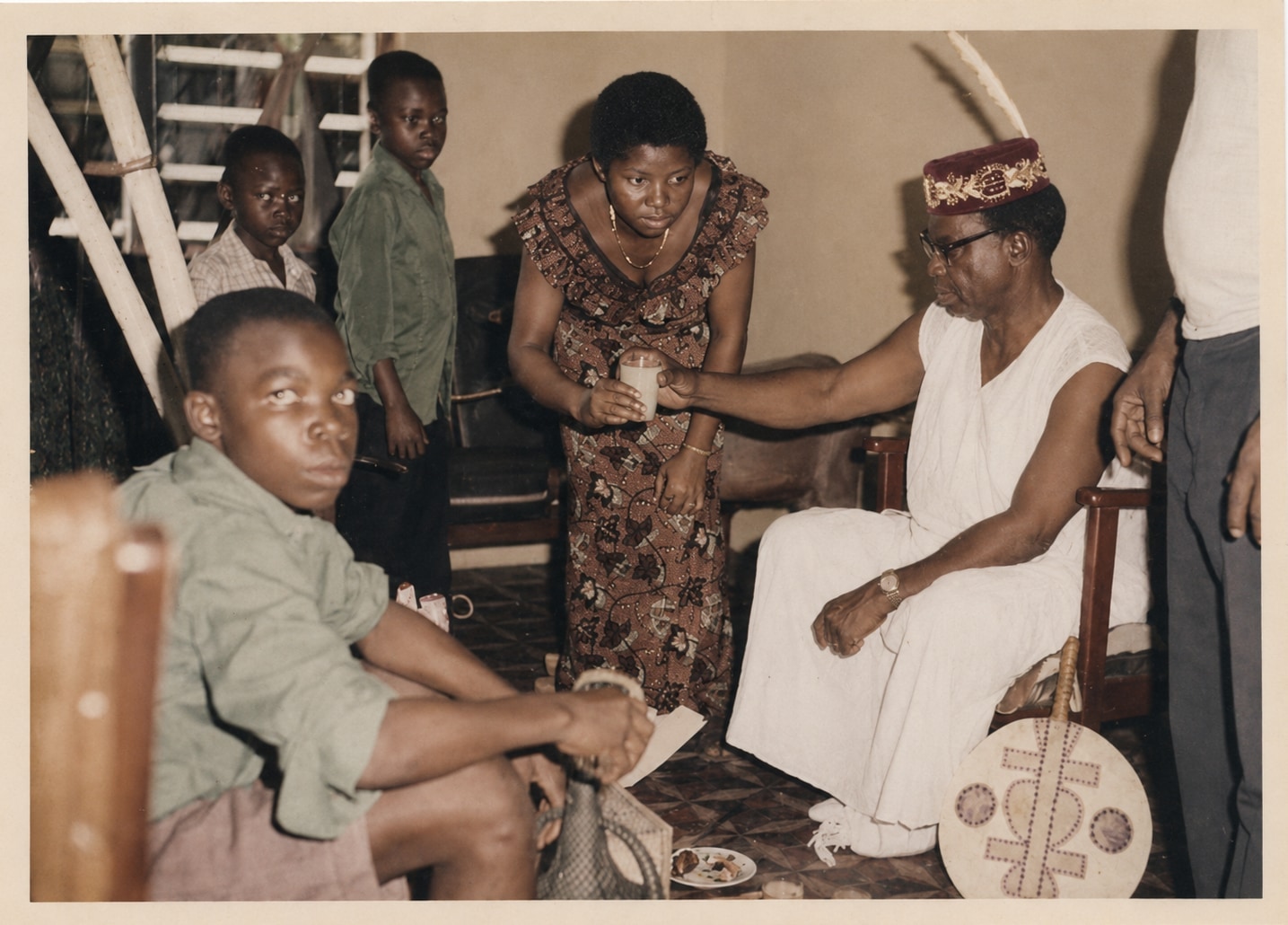 Oby's father seated outdoors in white with her mother and the children gathered around him