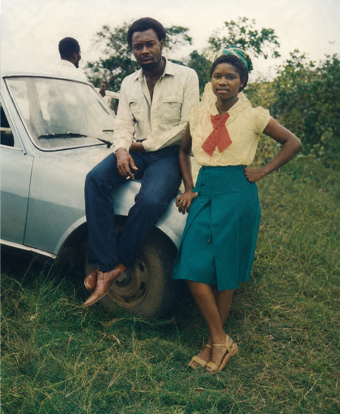 Oby standing beside her brother, who is seated on the bonnet of a car, on grass