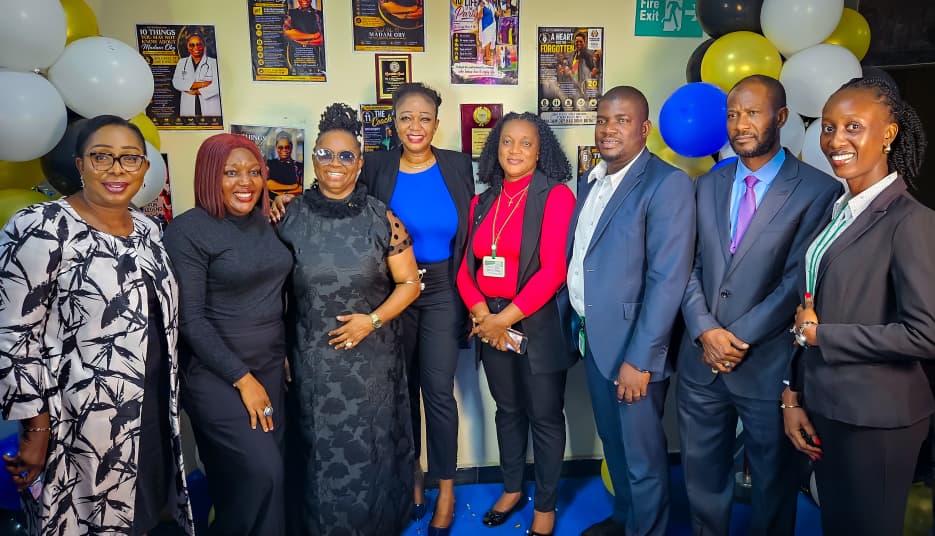 Eight colleagues standing with Dr. Oby Nwokedi in front of the poster wall