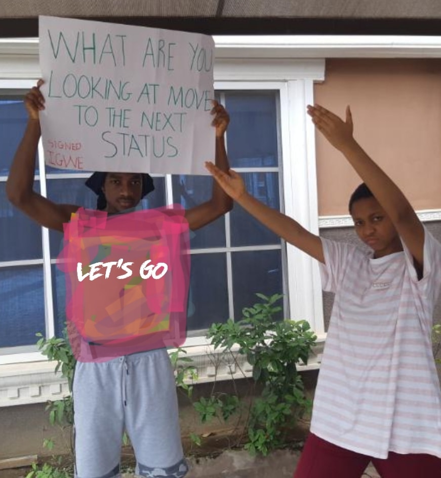 Two children outside a house, one holding up a hand-lettered sign