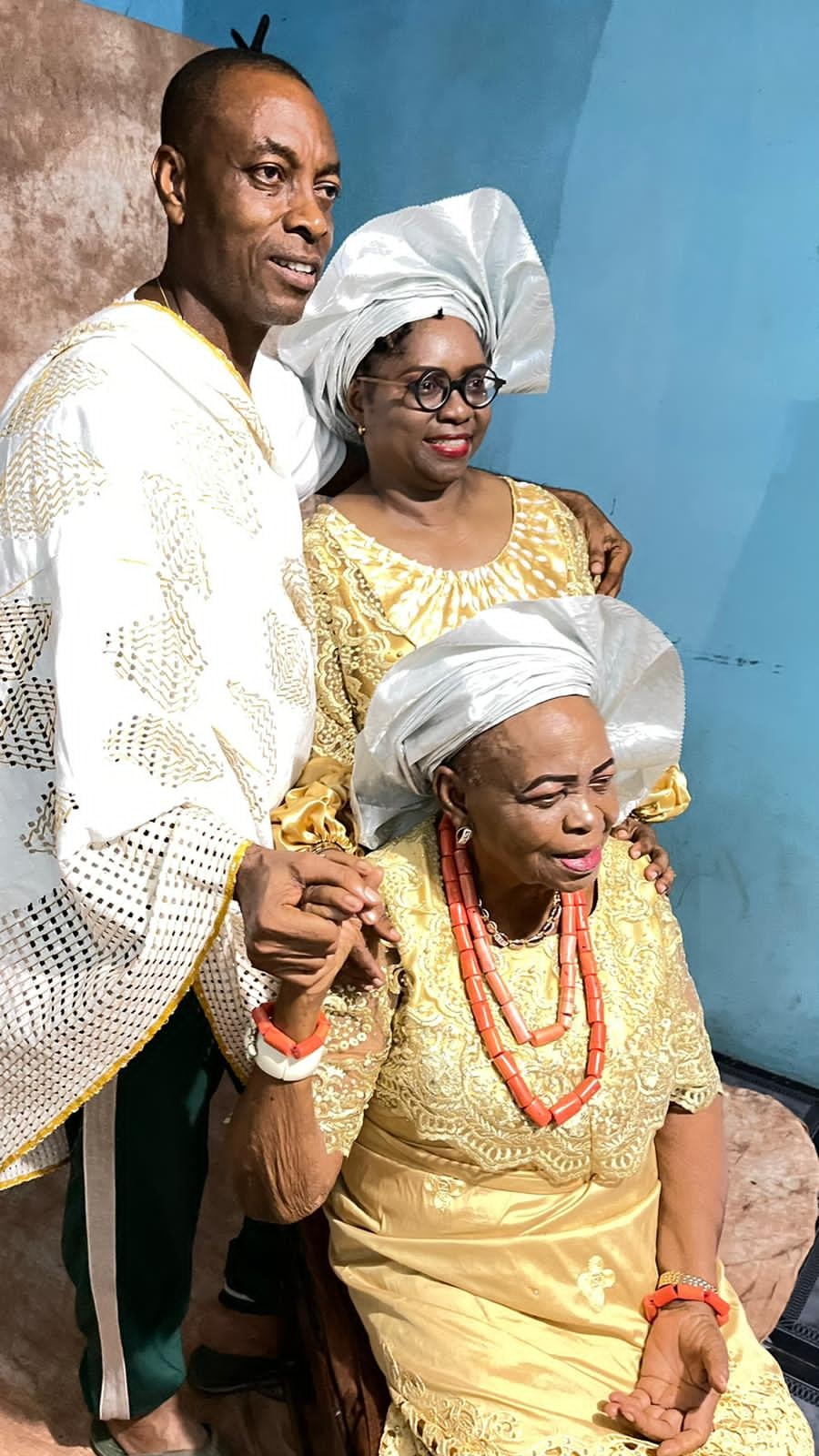 Dr. Oby Nwokedi and her husband standing behind an elder seated in gold and coral beads