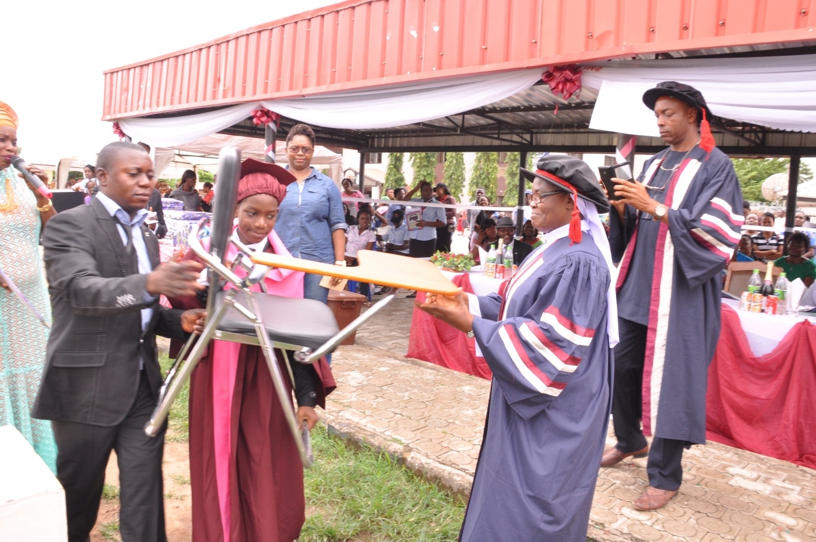 A gathering under a red canopy, several people in academic gowns and caps