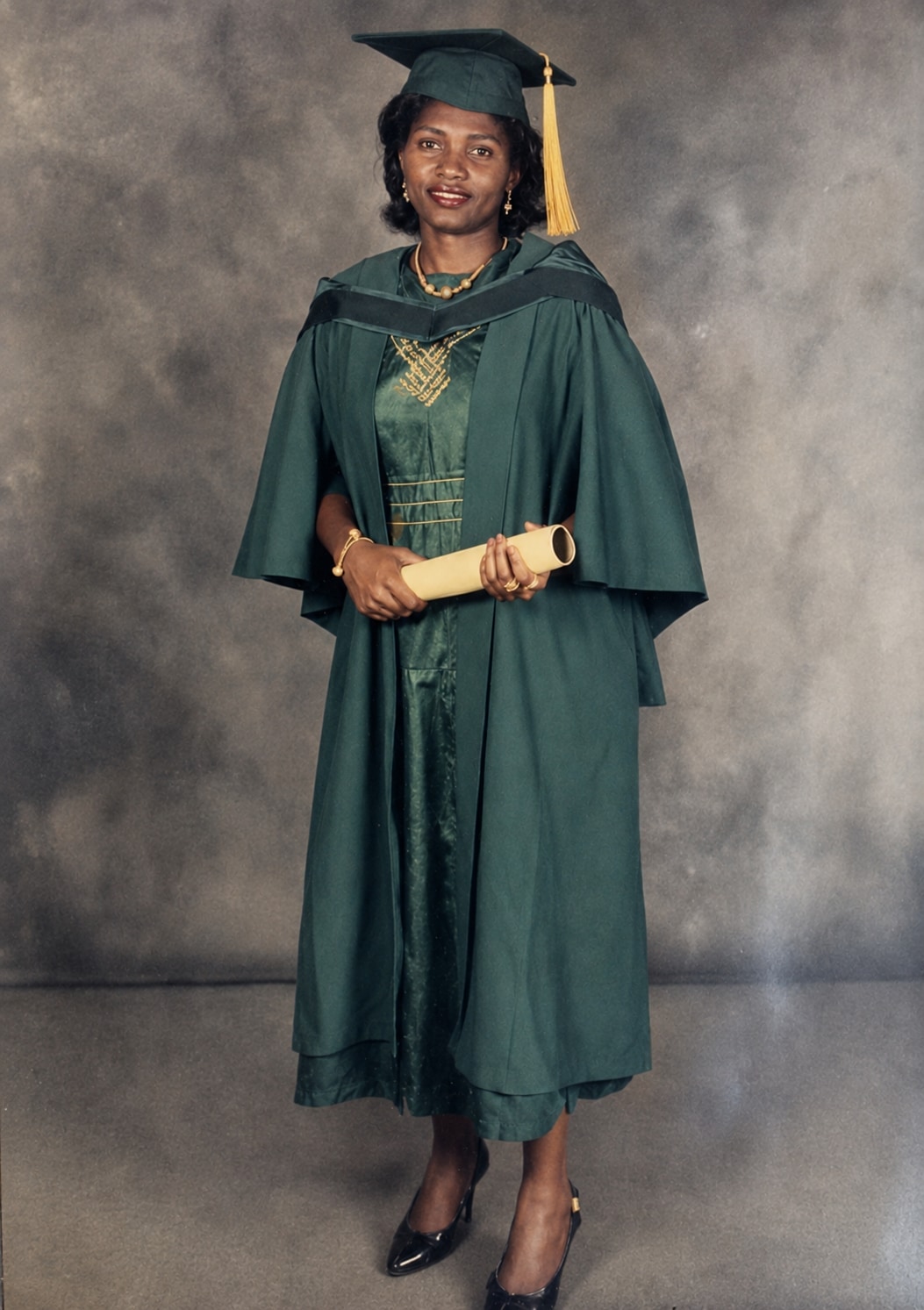 Oby Attoh in full green academic gown and hood, holding her scroll, at convocation