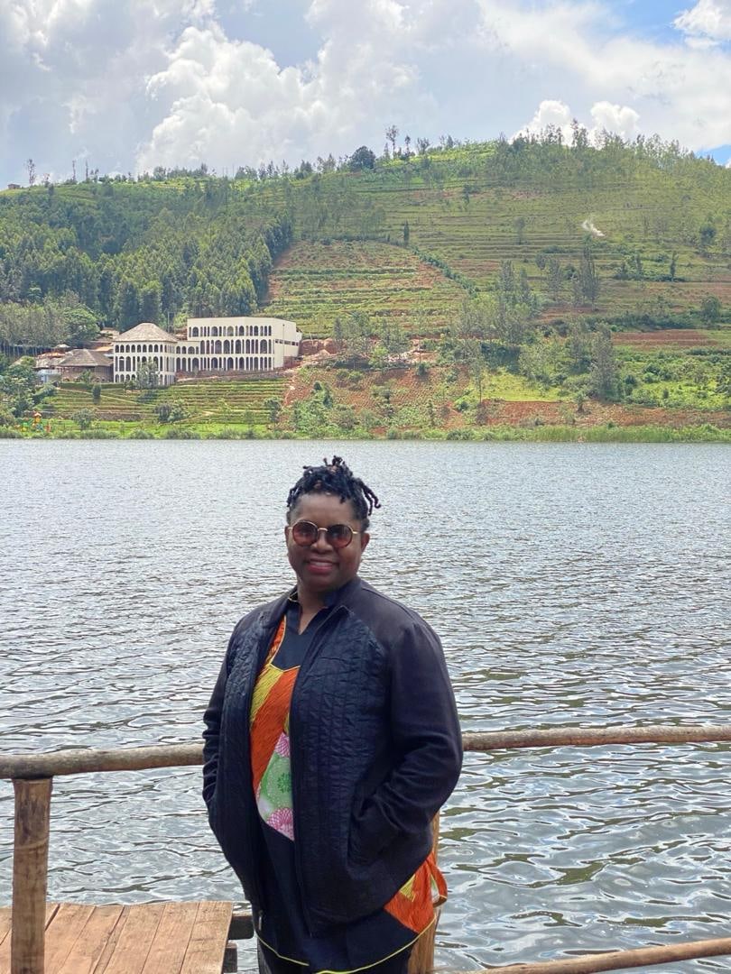 Dr. Oby Nwokedi standing at a lakeside railing with terraced green hills behind