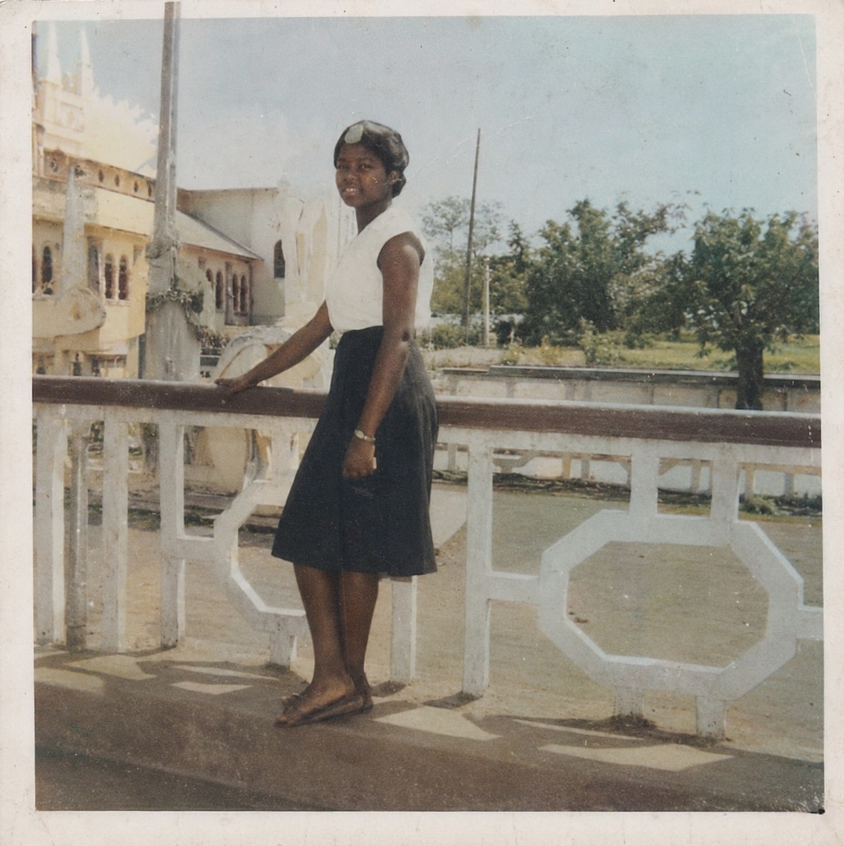 Oby Attoh in her secondary school uniform, a white blouse and dark skirt, standing on a balcony