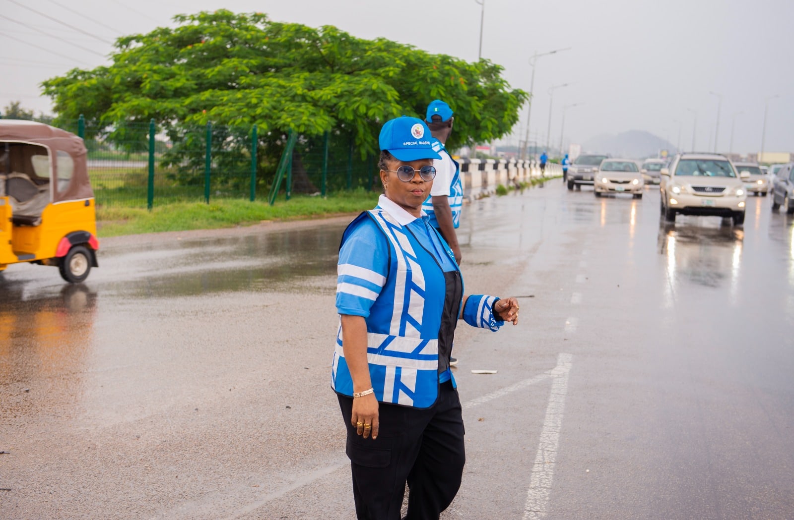 Dr. Oby Nwokedi standing on a wet highway in her Special Marshal vest, traffic approaching behind her
